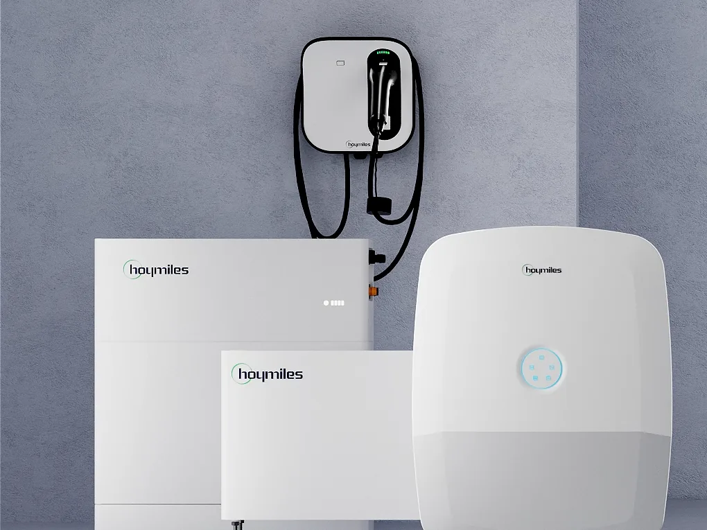Hoymiles HIT-Wechselrichter mit LED-Ring, zwei flache Speichermodule der Generation G2 und eine Hoymiles-Wallbox an einer grauen Wand